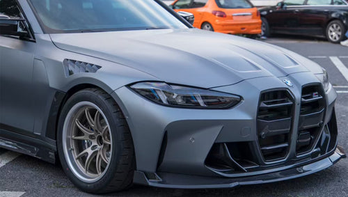 Close-up of a gray BMW G80 M3 featuring a REVOZPORT carbon fiber front lip, vented fenders, side skirts, and aggressive front aero styling in an outdoor parking lot.
