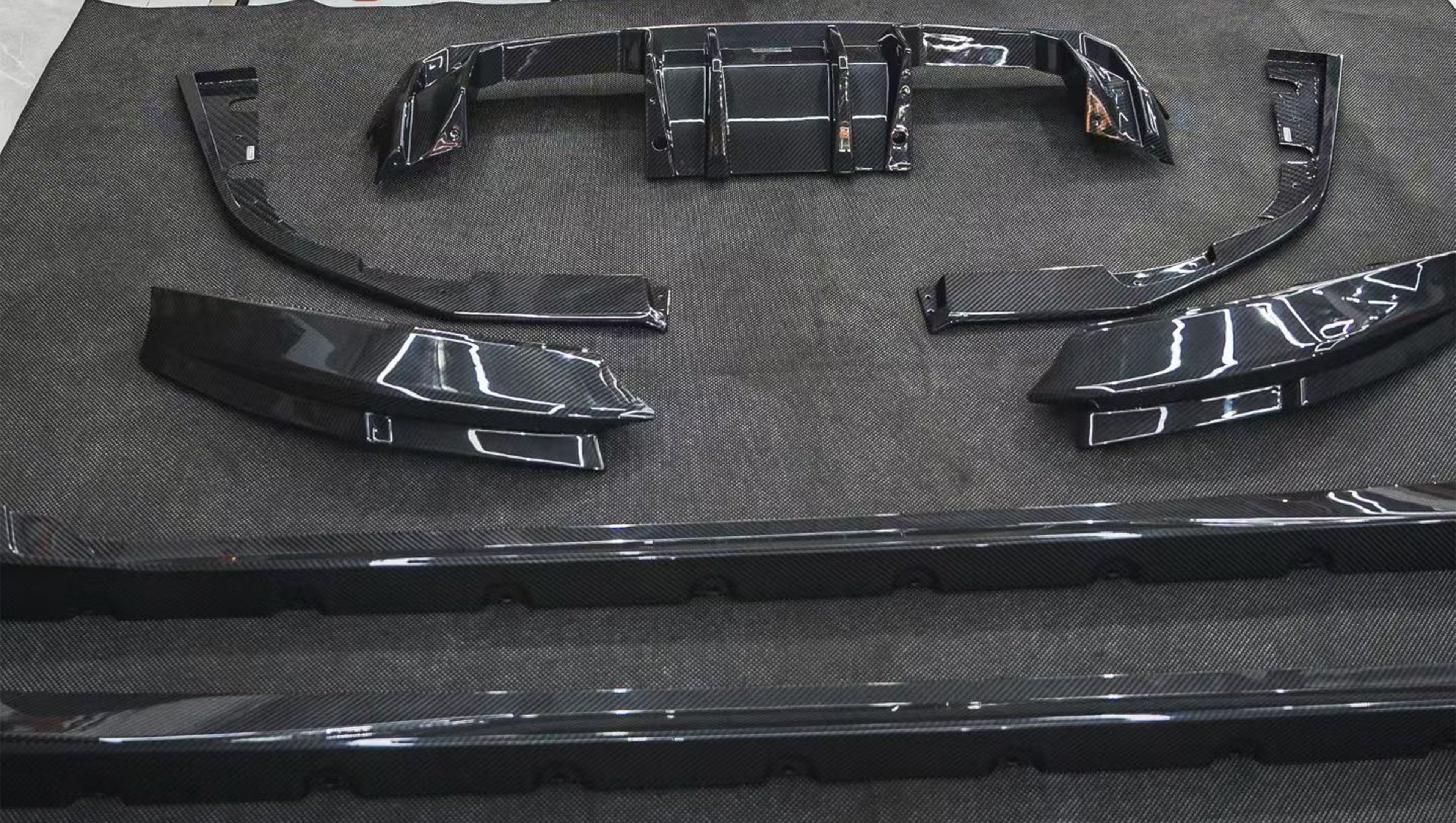 REVOZPORT glossy carbon fiber body kit components displayed before installation, including front lip sections, side skirts, rear diffuser, and aero trim pieces.