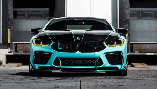 Turquoise BMW F92 M8 featuring a REVOZPORT carbon fiber body kit with front lip, side skirts, black hood accents, side vents, and silver forged wheels parked outside an industrial loading dock.
