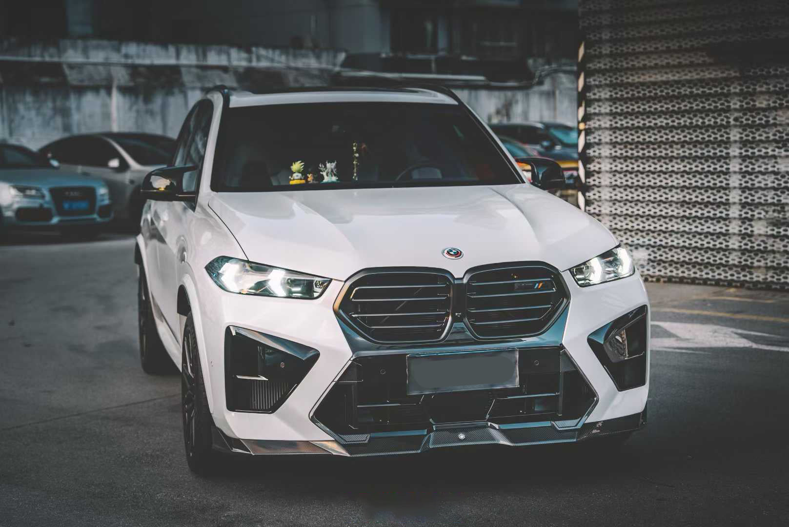 Front view of a white BMW X5M featuring a REVOZPORT carbon fiber front lip and aggressive front bumper aero styling parked on an urban street at night.
