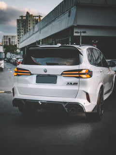 Front view of a white BMW X5M featuring a REVOZPORT carbon fiber front lip and aggressive front bumper aero styling parked on an urban street at night.