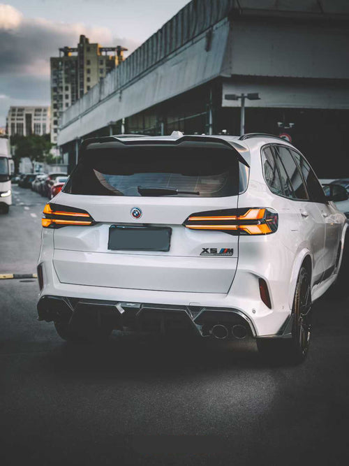 Front view of a white BMW X5M featuring a REVOZPORT carbon fiber front lip and aggressive front bumper aero styling parked on an urban street at night.