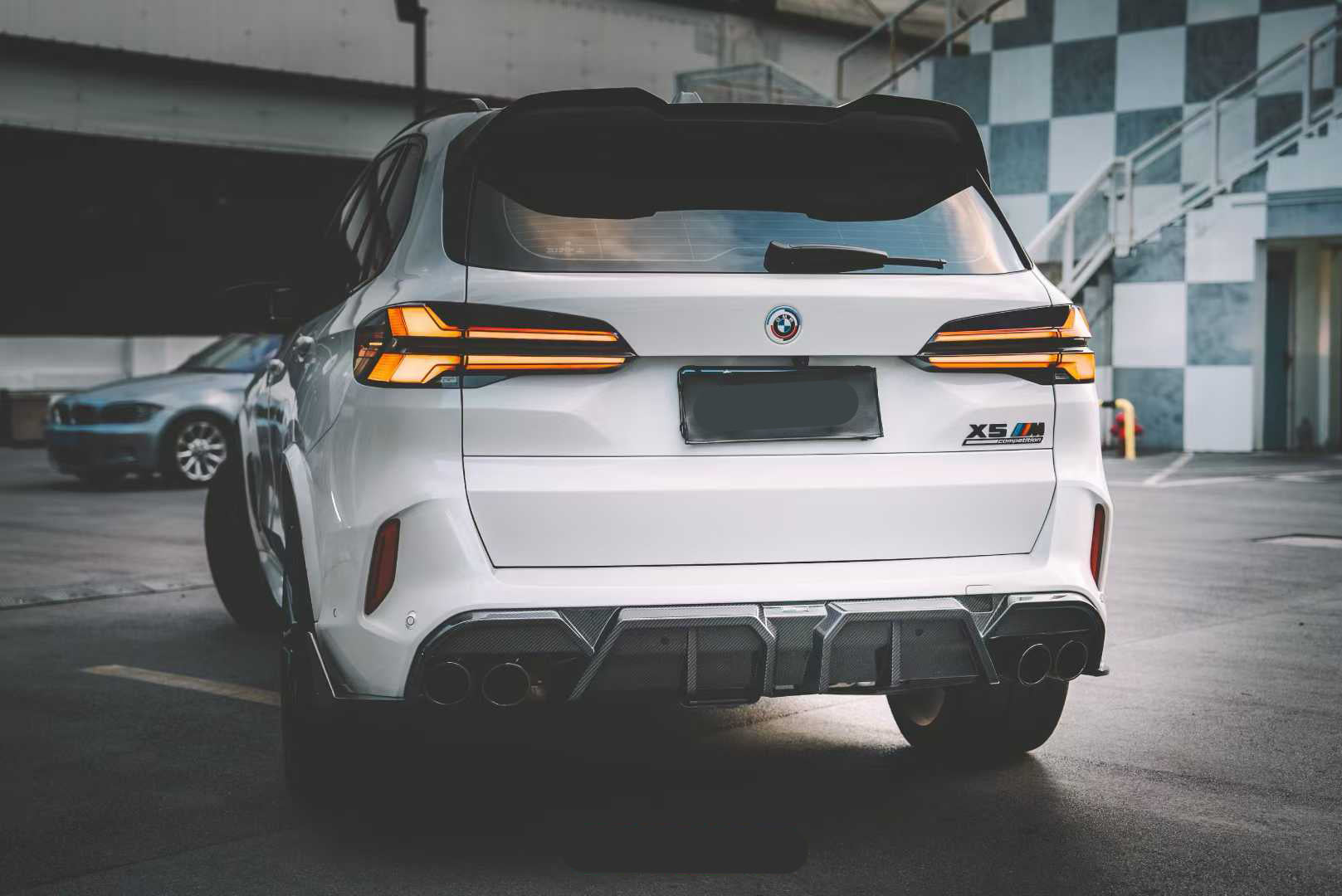 Front view of a white BMW X5M featuring a REVOZPORT carbon fiber front lip and aggressive front bumper aero styling parked on an urban street at night.