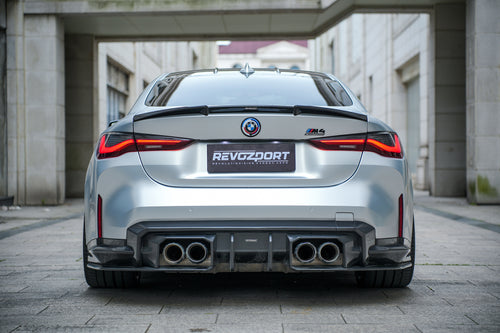 Silver BMW G82 M4 featuring a REVOZPORT carbon fiber body kit with front lip, side skirts, vented fenders, and aggressive aero styling parked in a modern urban courtyard.