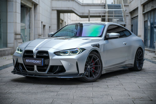 Silver BMW G82 M4 featuring a REVOZPORT carbon fiber body kit with front lip, side skirts, vented fenders, and aggressive aero styling parked in a modern urban courtyard.