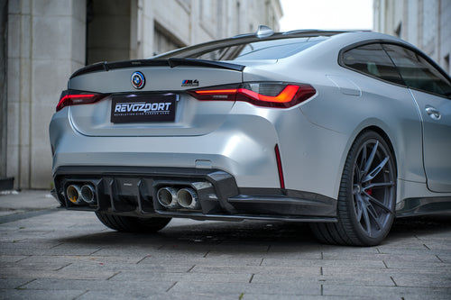 Silver BMW G82 M4 featuring a REVOZPORT carbon fiber body kit with front lip, side skirts, vented fenders, and aggressive aero styling parked in a modern urban courtyard.