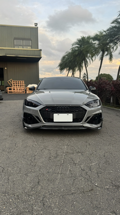 Gray Audi RS5 Sportback featuring a REVOZPORT carbon fiber front lip, side skirts, and aggressive front aero styling parked outdoors near tropical landscaping.