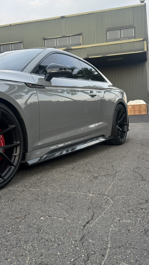 Gray Audi RS5 Sportback featuring a REVOZPORT carbon fiber front lip, side skirts, and aggressive front aero styling parked outdoors near tropical landscaping.