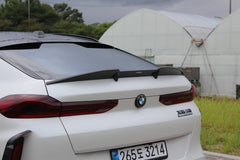 Front view of a white BMW X6M featuring an aggressive REVOZPORT front bumper and carbon fiber aero styling parked on a quiet urban street.