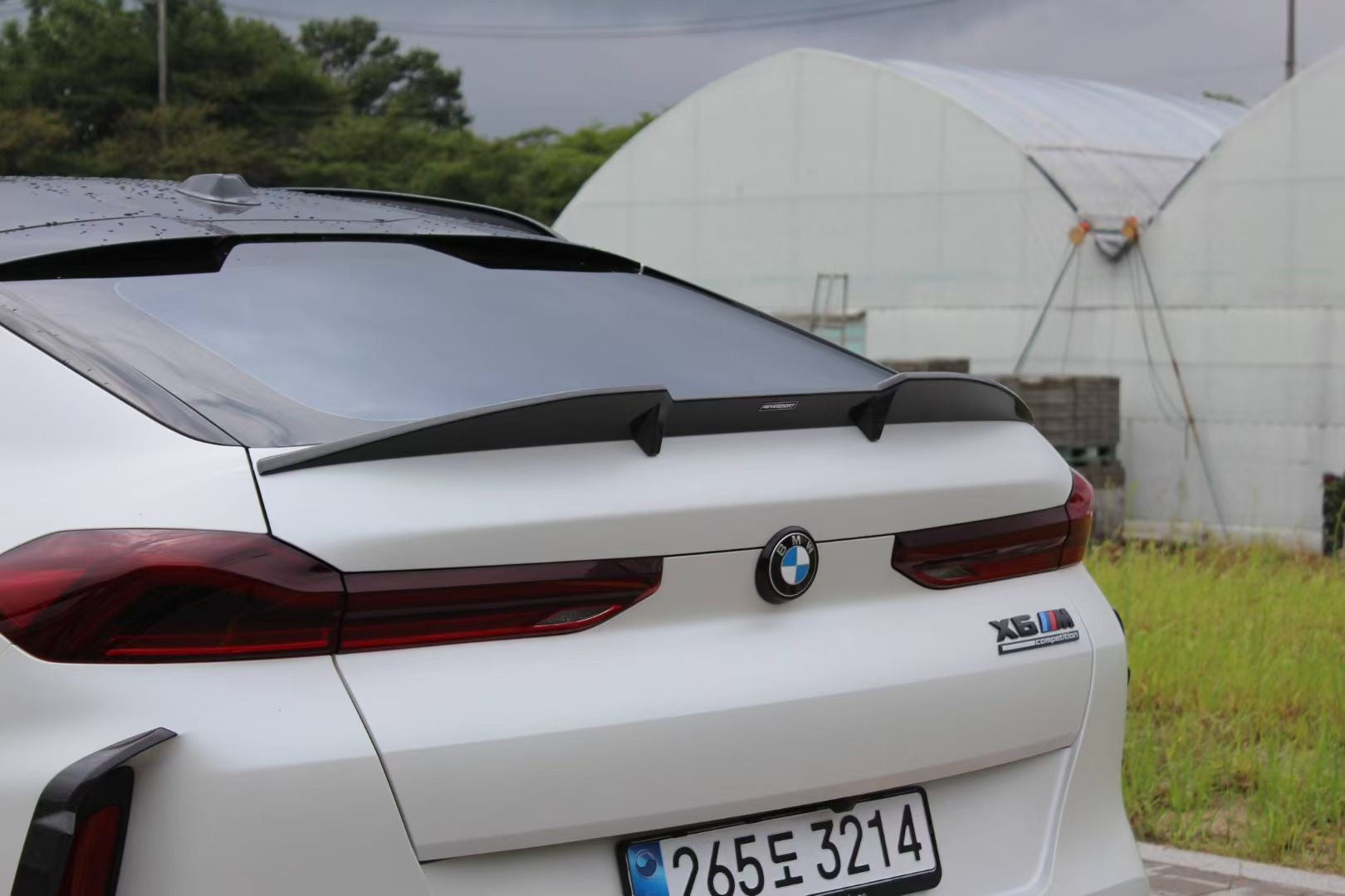 Front view of a white BMW X6M featuring an aggressive REVOZPORT front bumper and carbon fiber aero styling parked on a quiet urban street.