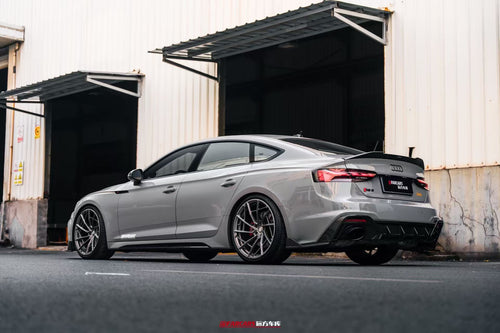 Gray Audi RS5 Sportback fitted with REVOZPORT forged multi-spoke wheels, parked outside an industrial garage.