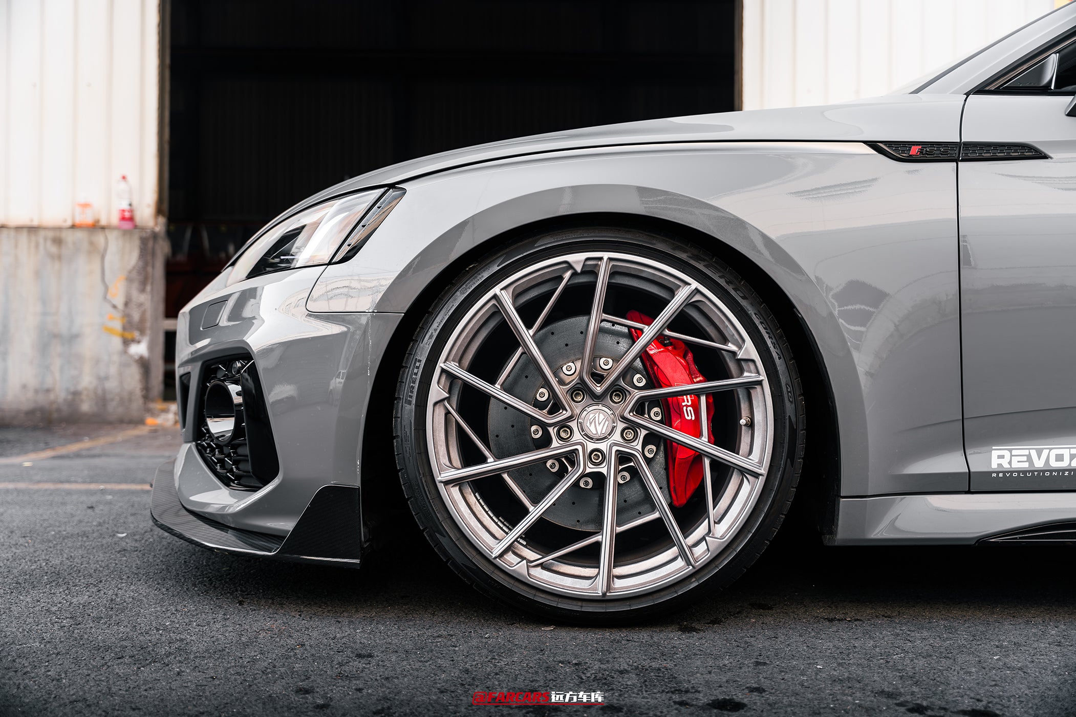 Gray Audi RS5 Sportback fitted with REVOZPORT forged multi-spoke wheels, parked outside an industrial garage.