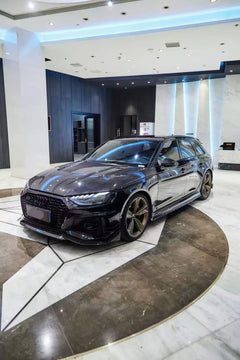 Black Audi RS4 Avant featuring a REVOZPORT carbon fiber body kit with front lip, side skirts, and aggressive aero styling displayed inside a luxury showroom.