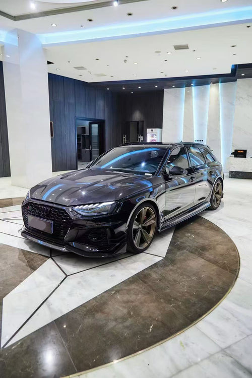 Black Audi RS4 Avant featuring a REVOZPORT carbon fiber body kit with front lip, side skirts, and aggressive aero styling displayed inside a luxury showroom.