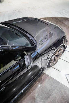Black Audi RS4 Avant featuring a REVOZPORT carbon fiber body kit with front lip, side skirts, and aggressive aero styling displayed inside a luxury showroom.