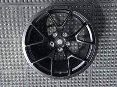 Studio-style close-up of a matte black forged performance wheel featuring a lightweight multi-spoke design and REVOZPORT branding. The wheel is displayed on a textured industrial floor, highlighting its premium finish, deep concave profile, and motorsport-inspired styling.