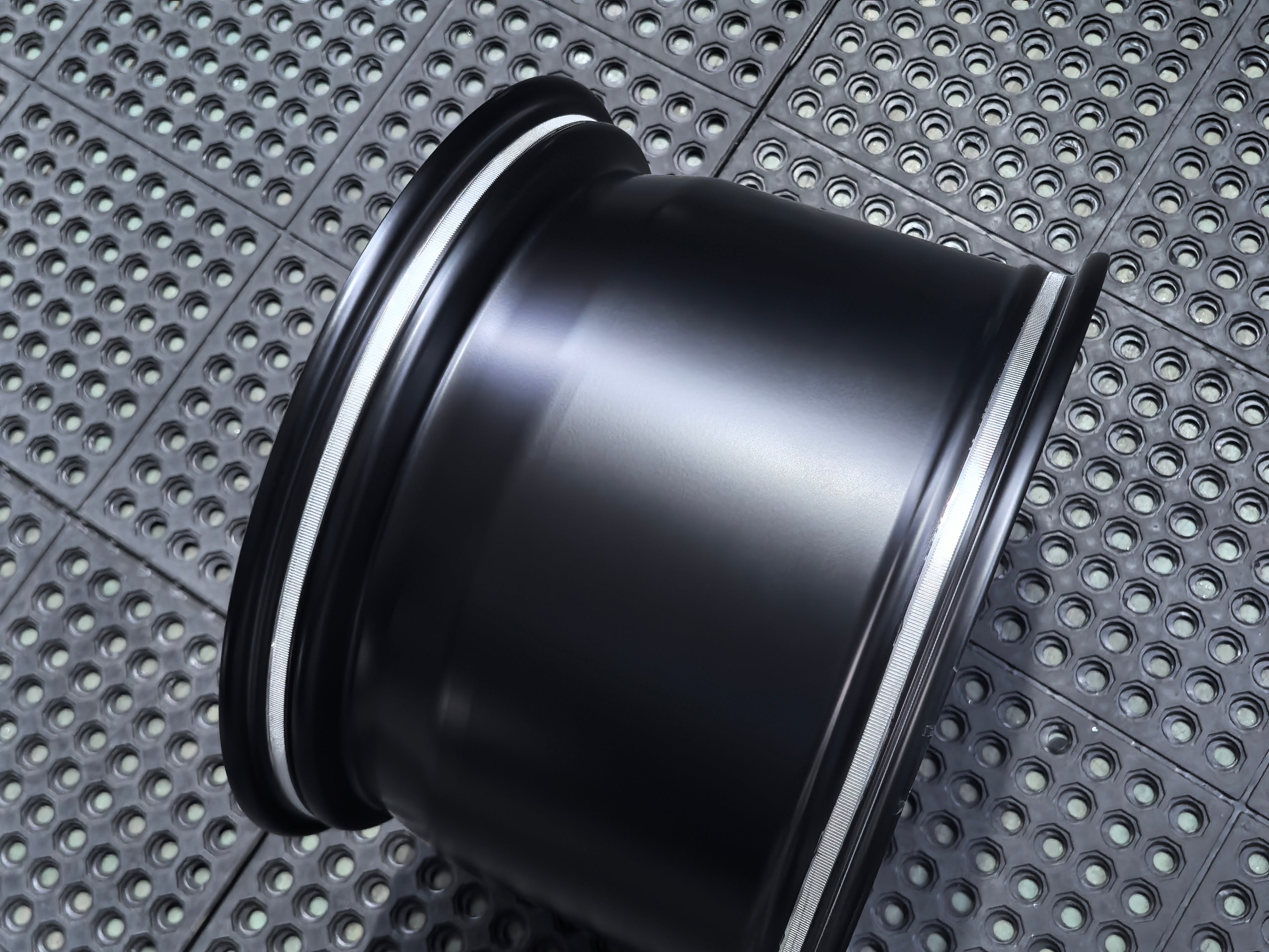 Studio-style close-up of a matte black forged performance wheel featuring a lightweight multi-spoke design and REVOZPORT branding. The wheel is displayed on a textured industrial floor, highlighting its premium finish, deep concave profile, and motorsport-inspired styling.