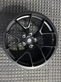 Studio-style close-up of a matte black forged performance wheel featuring a lightweight multi-spoke design and REVOZPORT branding. The wheel is displayed on a textured industrial floor, highlighting its premium finish, deep concave profile, and motorsport-inspired styling.