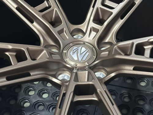 Bronze REVOZPORT forged alloy wheel with an intricate split multi-spoke design displayed on a black textured workshop floor.