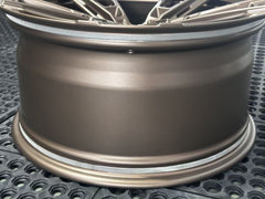 Bronze REVOZPORT forged alloy wheel with an intricate split multi-spoke design displayed on a black textured workshop floor.