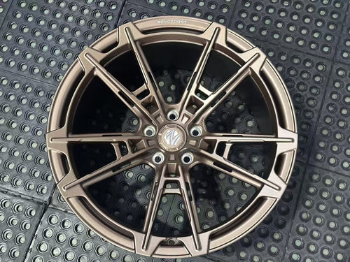 Bronze REVOZPORT forged alloy wheel with an intricate split multi-spoke design displayed on a black textured workshop floor.