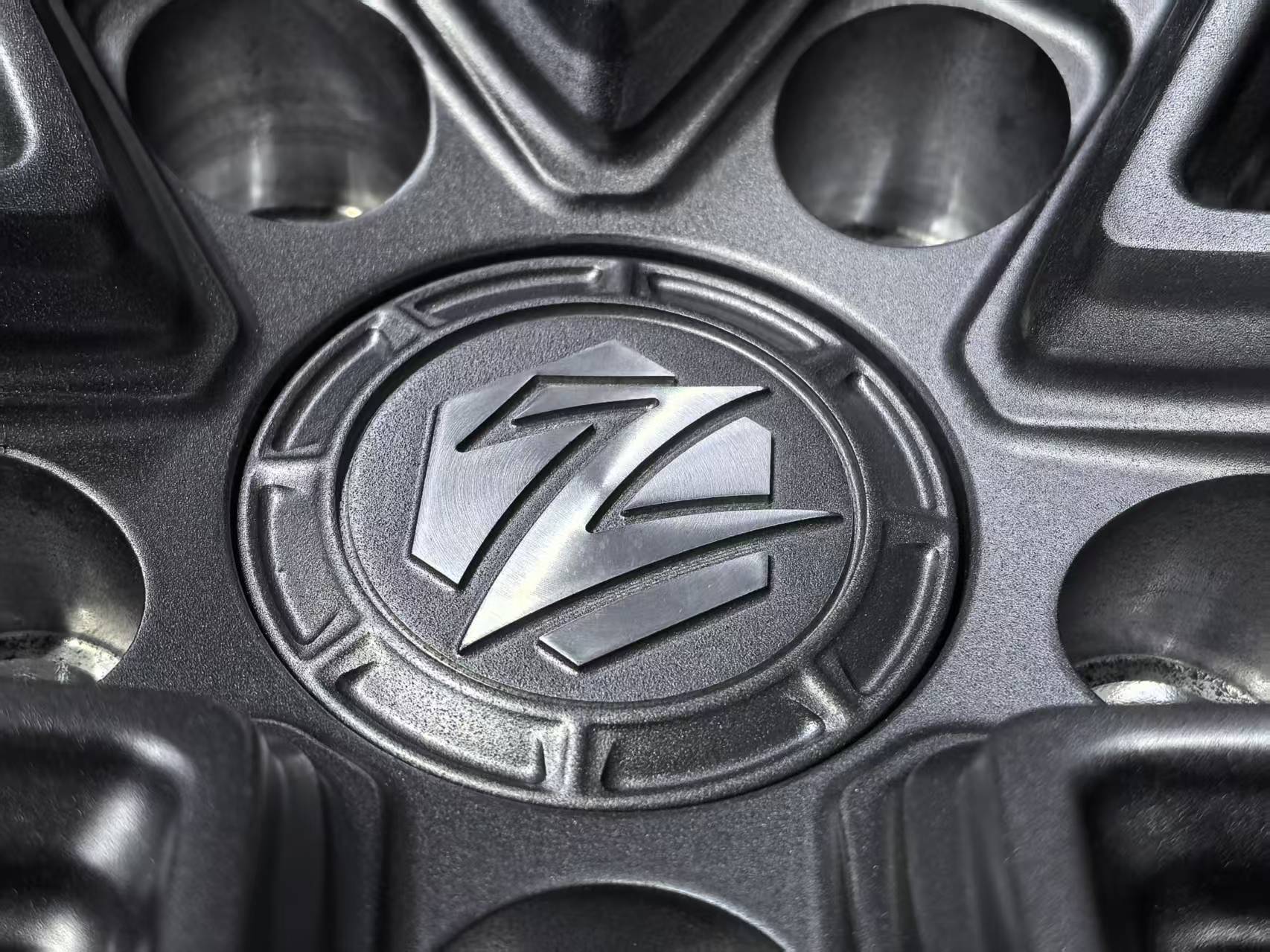 Matte gray REVOZPORT forged alloy wheel with an intricate split multi-spoke design displayed on a black textured workshop floor.