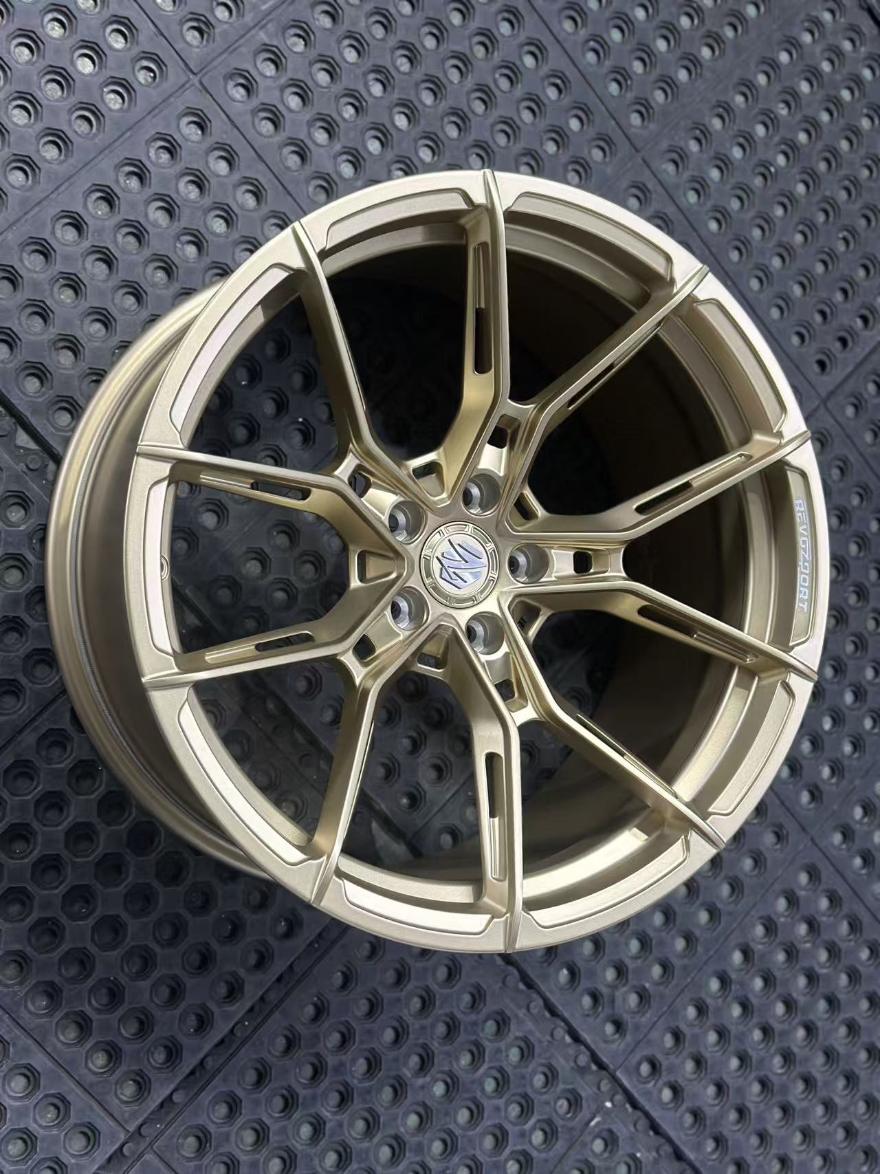 Bronze REVOZPORT forged alloy wheel with split multi-spoke design displayed on a black textured workshop floor.