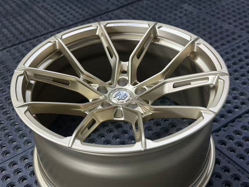 Bronze REVOZPORT forged alloy wheel with split multi-spoke design displayed on a black textured workshop floor.