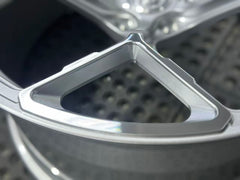 Silver forged alloy wheel with a multi-spoke design displayed against a black textured rubber floor.