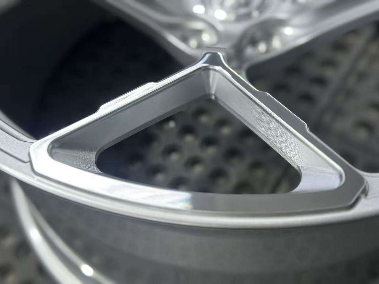Silver forged alloy wheel with a multi-spoke design displayed against a black textured rubber floor.