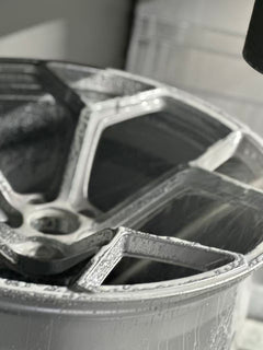 Silver forged alloy wheel with a multi-spoke design displayed against a black textured rubber floor.