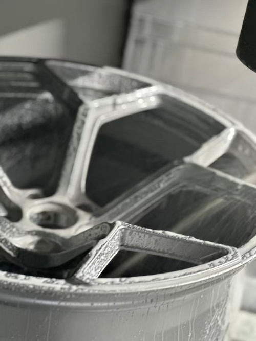 Silver forged alloy wheel with a multi-spoke design displayed against a black textured rubber floor.