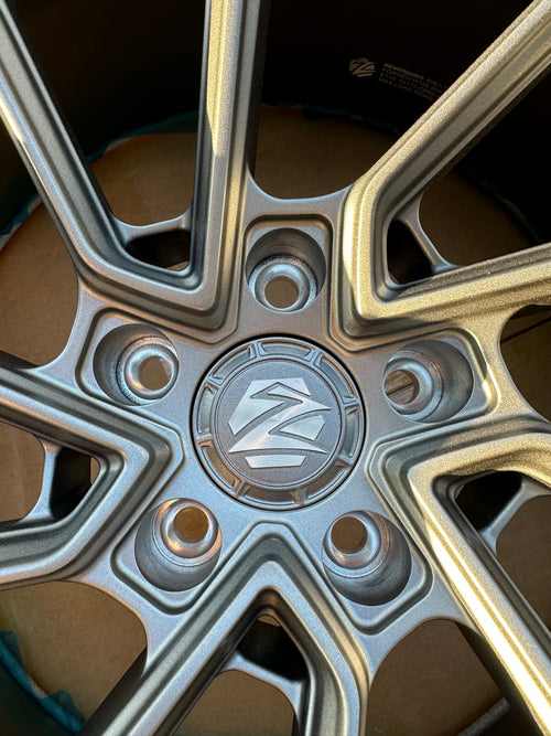 Matte gray REVOZPORT forged alloy wheel with an intricate split multi-spoke design displayed on a black textured workshop floor.