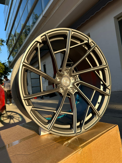 Matte gray REVOZPORT forged alloy wheel with an intricate split multi-spoke design displayed on a black textured workshop floor.