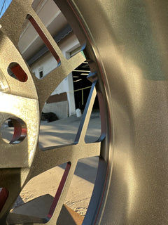 Matte gray REVOZPORT forged alloy wheel with an intricate split multi-spoke design displayed on a black textured workshop floor.