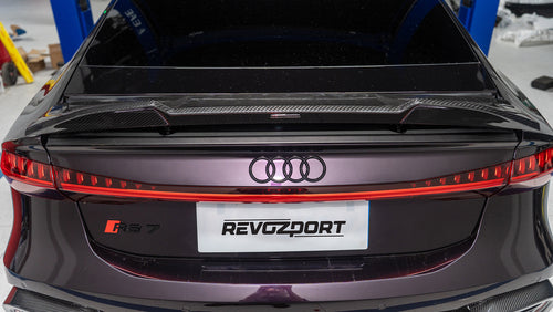 Black Audi RS7 featuring a REVOZPORT carbon fiber body kit with front lip, side skirts, carbon hood, and aggressive aero styling driving on a city street.