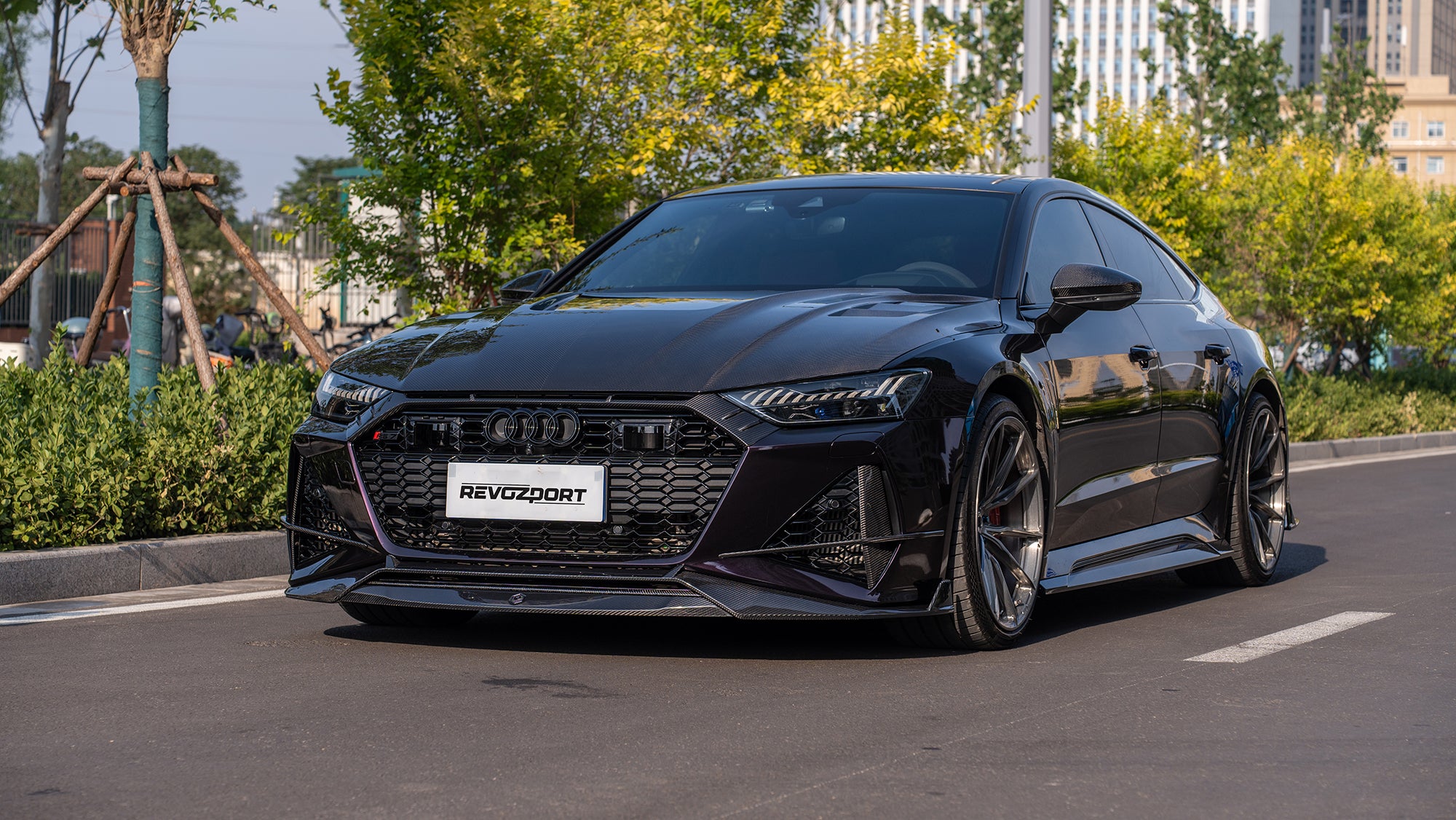 Black Audi RS7 featuring a REVOZPORT carbon fiber body kit with front lip, side skirts, carbon hood, and aggressive aero styling driving on a city street.