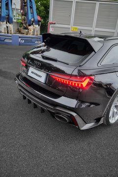Black Audi RS6 Avant fitted with a REVOZPORT body kit and silver multi-spoke wheels, parked in an open lot surrounded by trees.