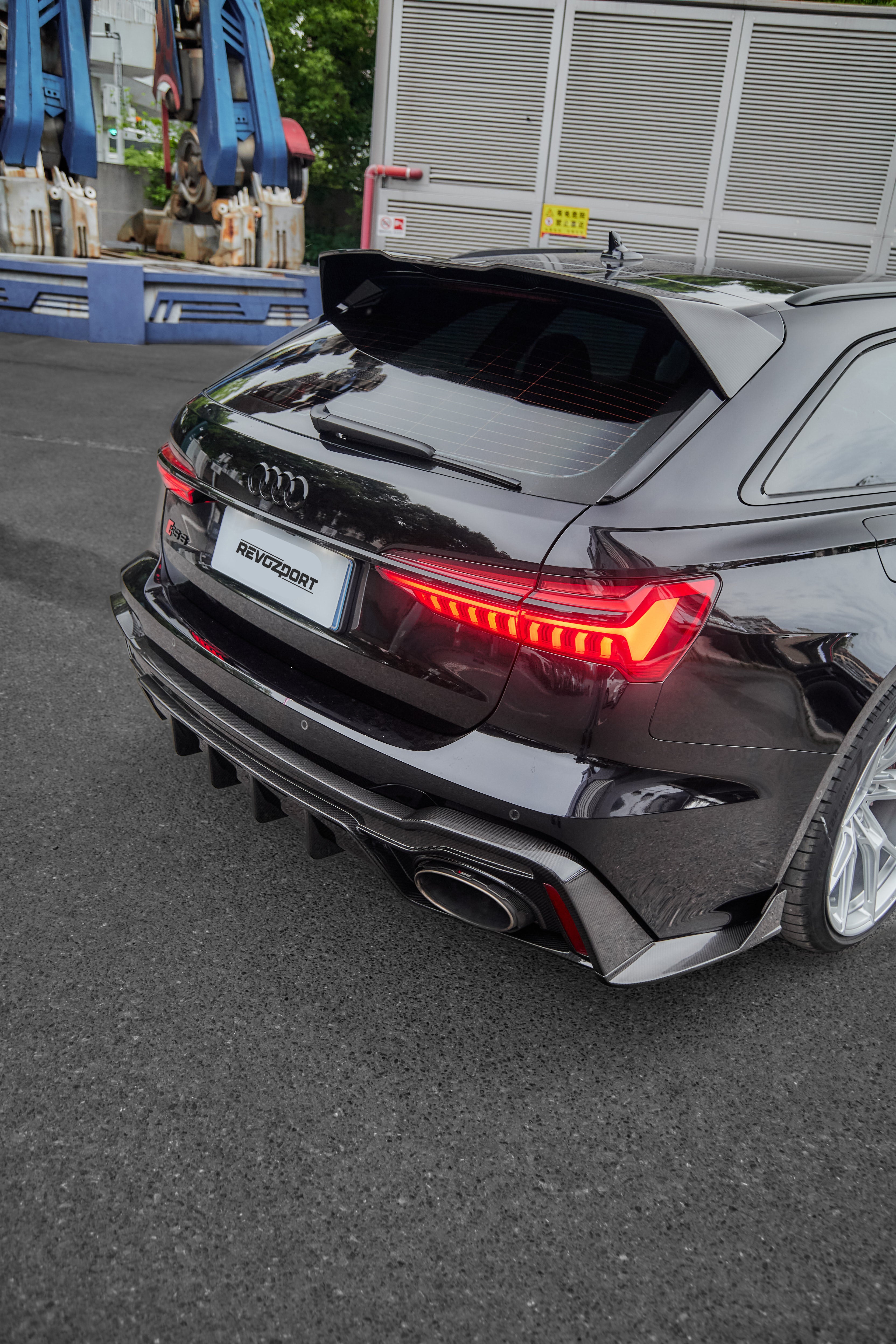 Black Audi RS6 Avant fitted with a REVOZPORT body kit and silver multi-spoke wheels, parked in an open lot surrounded by trees.