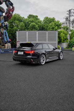 Black Audi RS6 Avant fitted with a REVOZPORT body kit and silver multi-spoke wheels, parked in an open lot surrounded by trees.