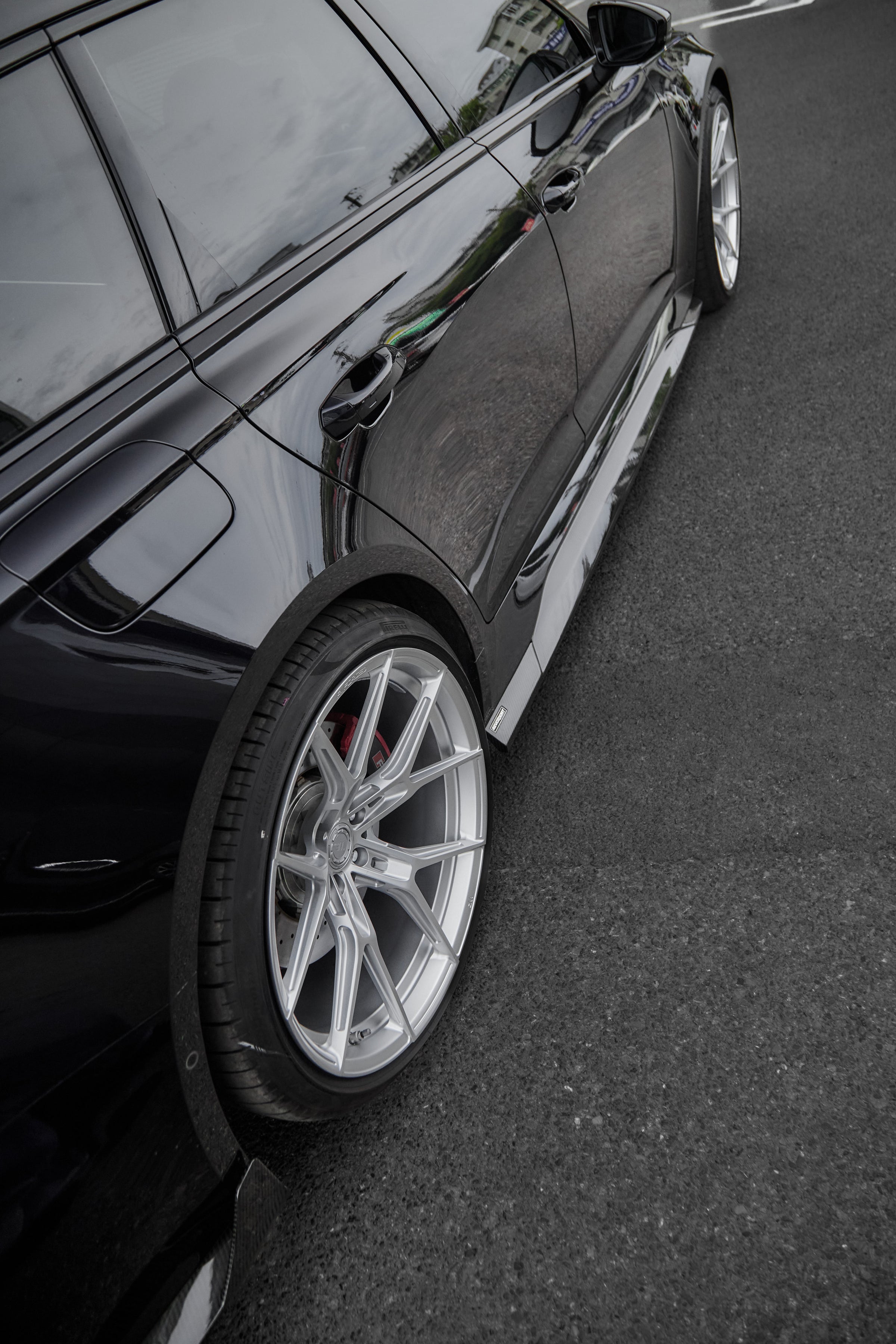 Black Audi RS6 Avant fitted with a REVOZPORT body kit and silver multi-spoke wheels, parked in an open lot surrounded by trees.