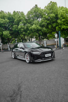 Black Audi RS6 Avant fitted with a REVOZPORT body kit and silver multi-spoke wheels, parked in an open lot surrounded by trees.