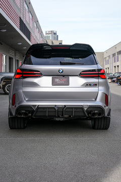 Gray BMW X5M featuring a REVOZPORT carbon fiber body kit with aggressive front lip, side skirts, and sporty aero styling parked outside a workshop.