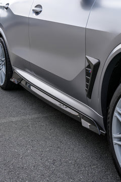 Gray BMW X5M featuring a REVOZPORT carbon fiber body kit with aggressive front lip, side skirts, and sporty aero styling parked outside a workshop.