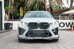 Front-facing view of a white BMW featuring aggressive carbon fiber front aero, illuminated headlights, sharp intake details, and performance-focused styling.