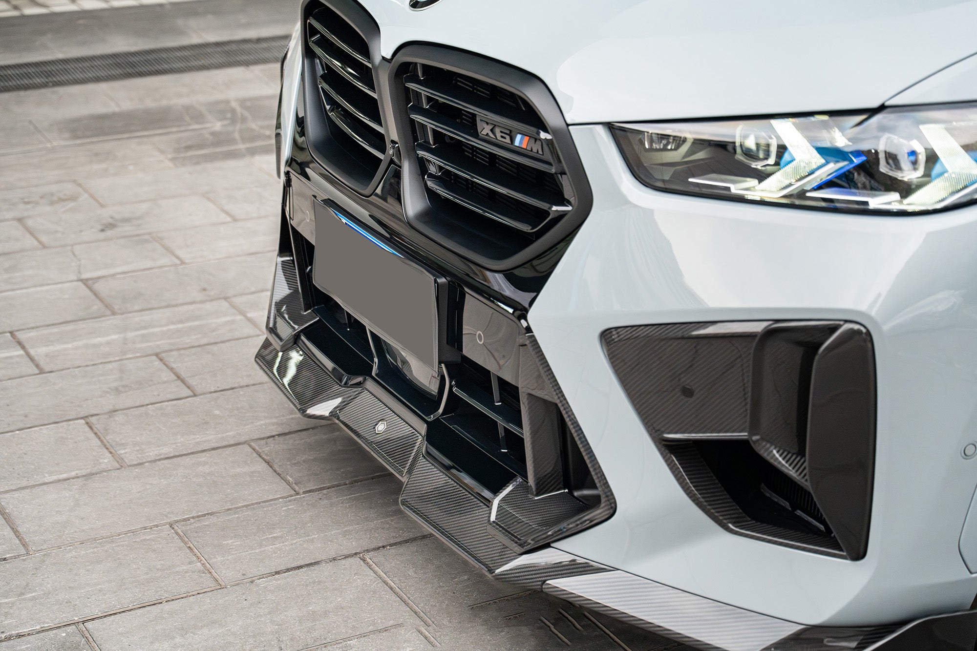 Detailed carbon fiber front aero close-up featuring aggressive splitter elements, precision vent design, and high-gloss composite surfaces under clean workshop lighting.