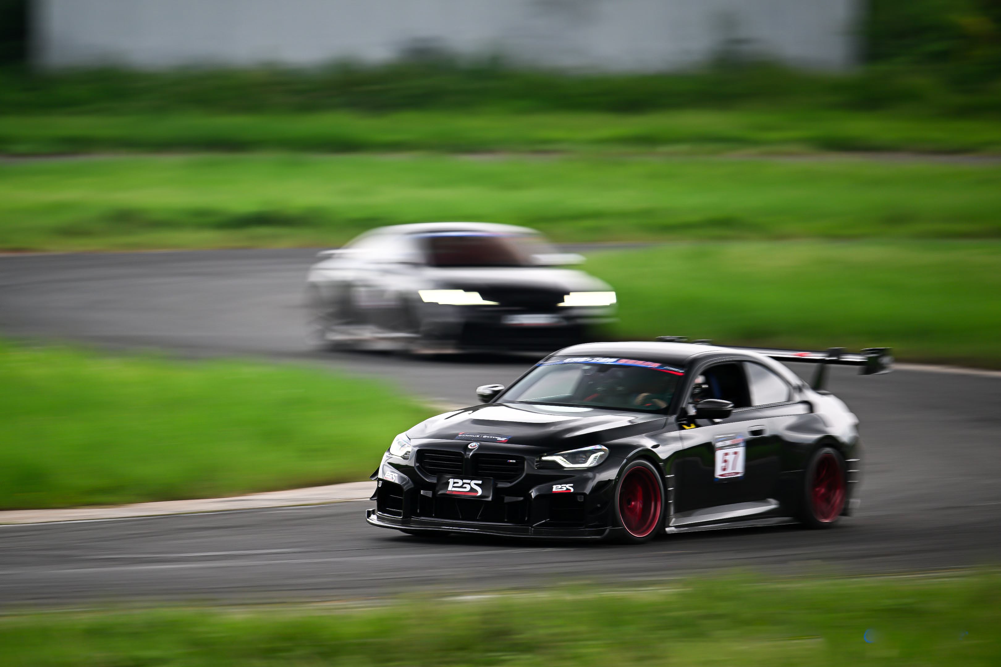 Rolling shot of a black BMW on racetrack, featuring oversized rear wing, aggressive carbon fiber aero, lowered stance, and motorsport wheel setup.