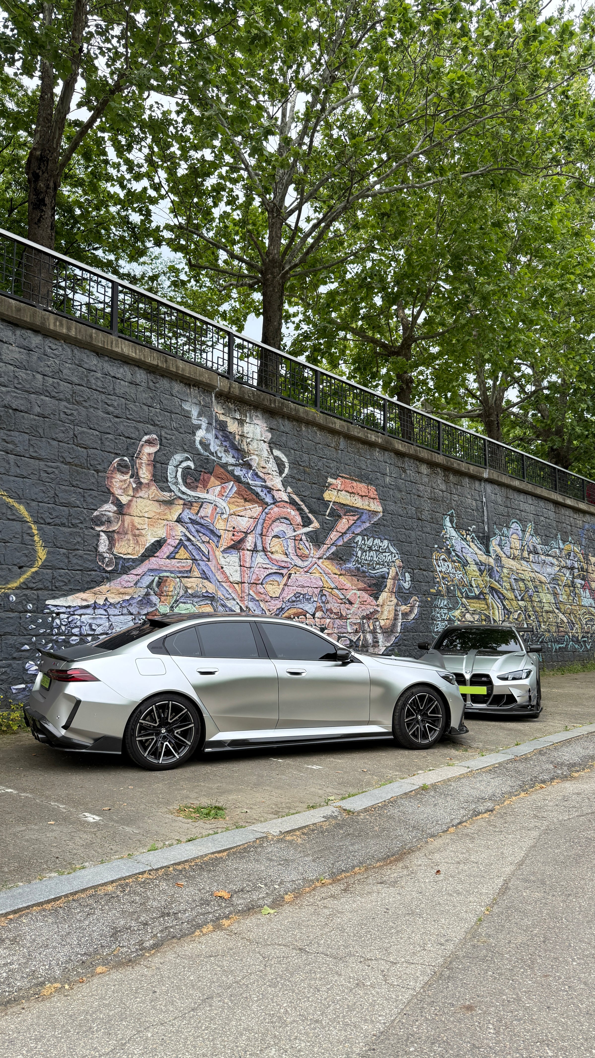 Top-down view of two BMWs with carbon fiber aero kits, hood vents, and rear wing parked beside a quiet road.