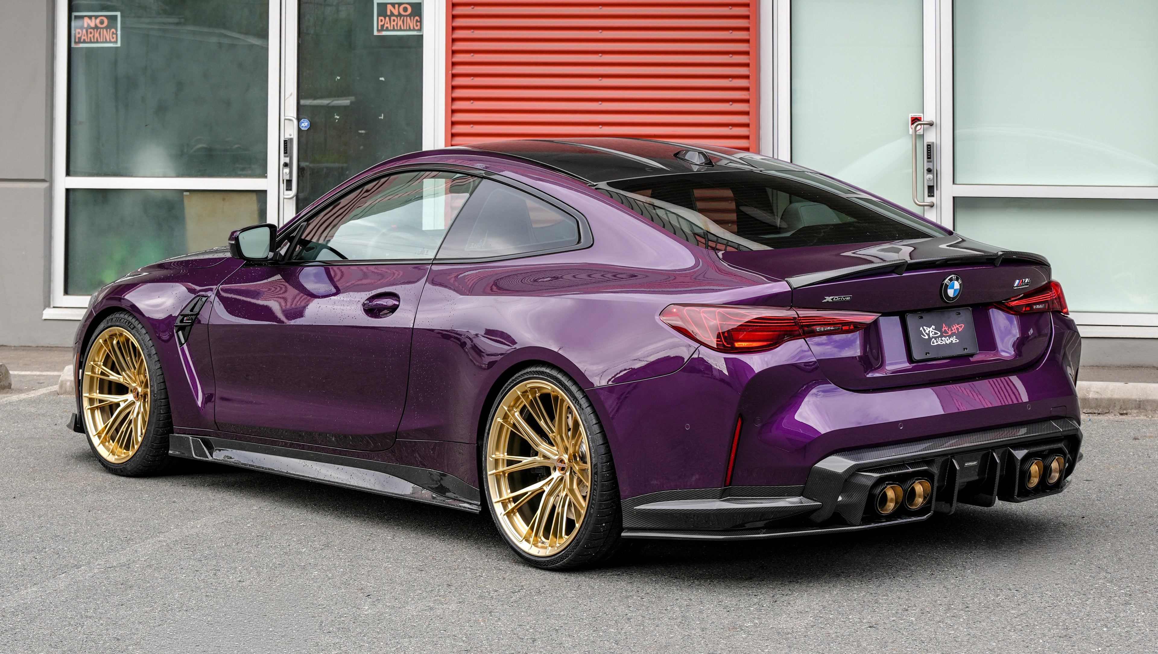 Purple BMW G82 M4 featuring a REVOZPORT carbon fiber body kit with front lip, side skirts, vented fenders, and gold wheels parked outside a modern industrial building.