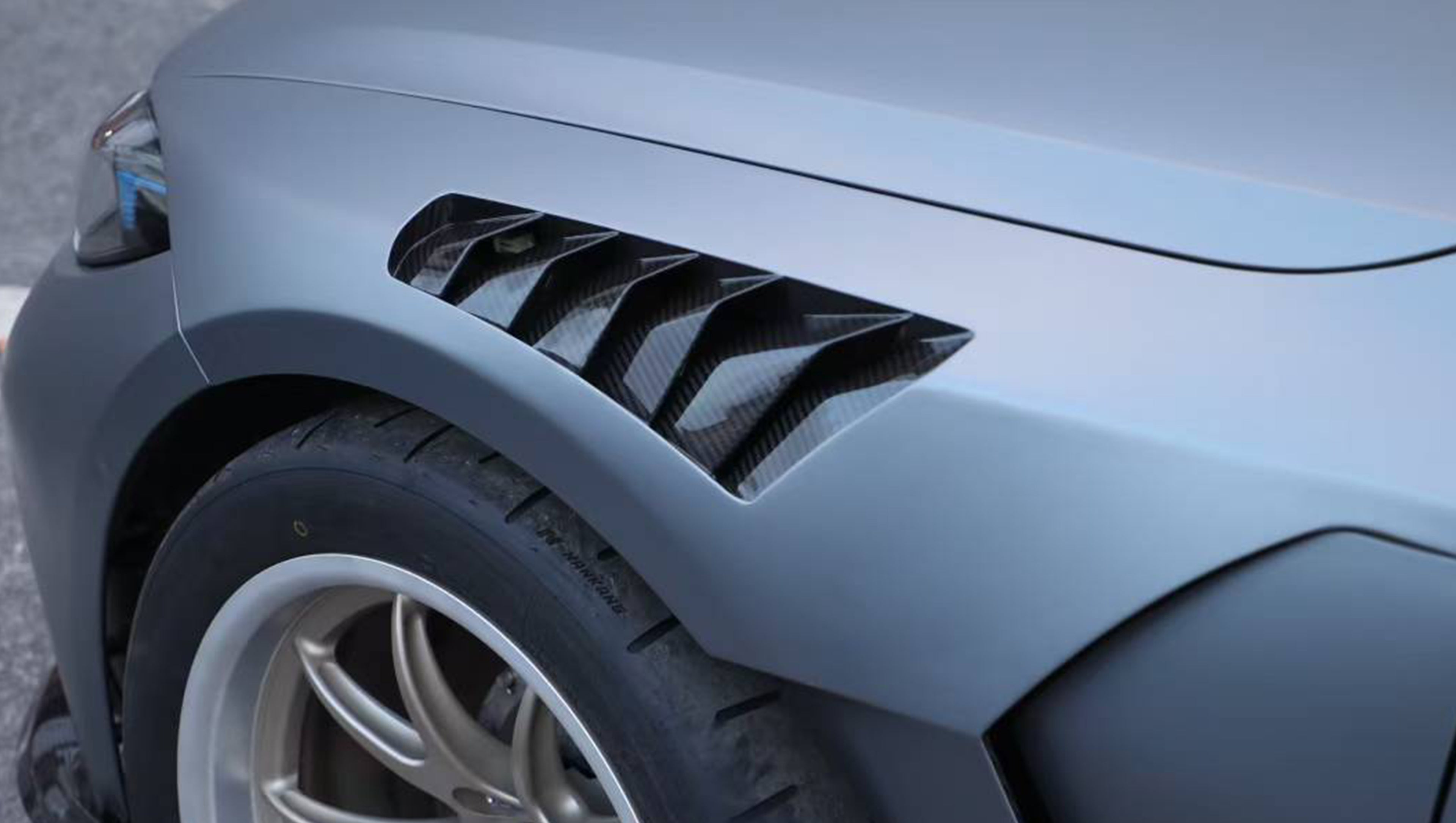 Close-up of a gray BMW G80 M3 featuring a REVOZPORT carbon fiber front lip, vented fenders, side skirts, and aggressive front aero styling in an outdoor parking lot.